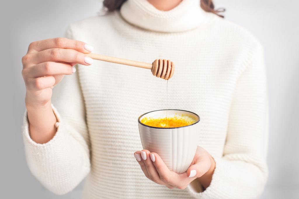 Eine Frau gibt Honig zu einer Tasse mit Goldener Milch.