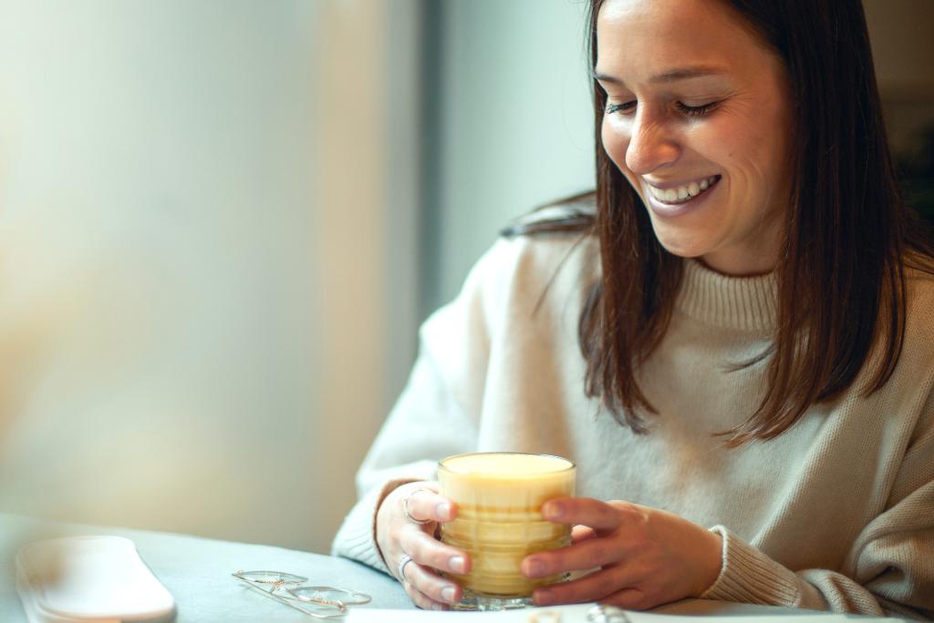 Eine glückliche Frau mit einem Glas Goldener Milch.