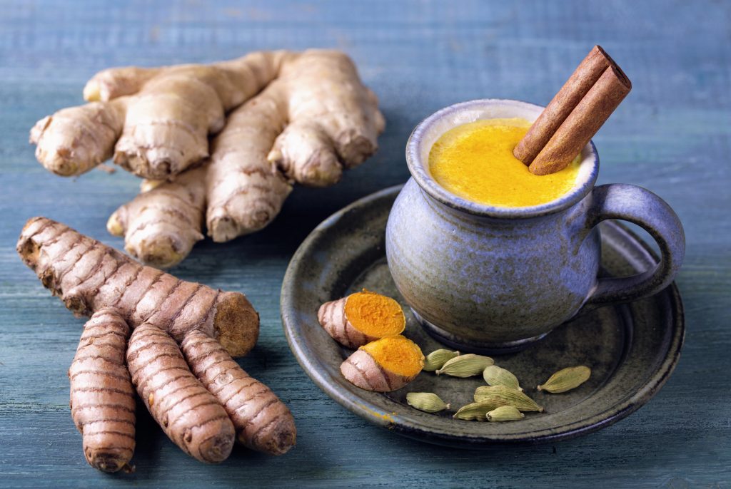 Goldene Milch in einer blauen Tontasse neben zwei Ingwer Wurzeln - Ayurveda zum Abnehmen