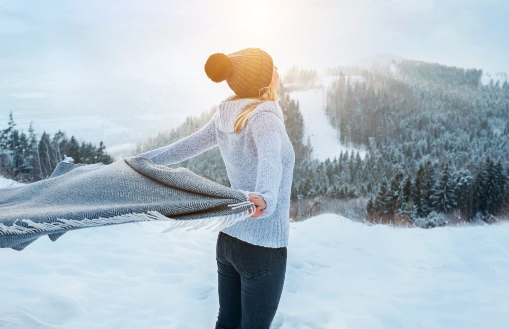 Eine Frau genießt die winterliche Sonne in schneebedeckter Landschaft.