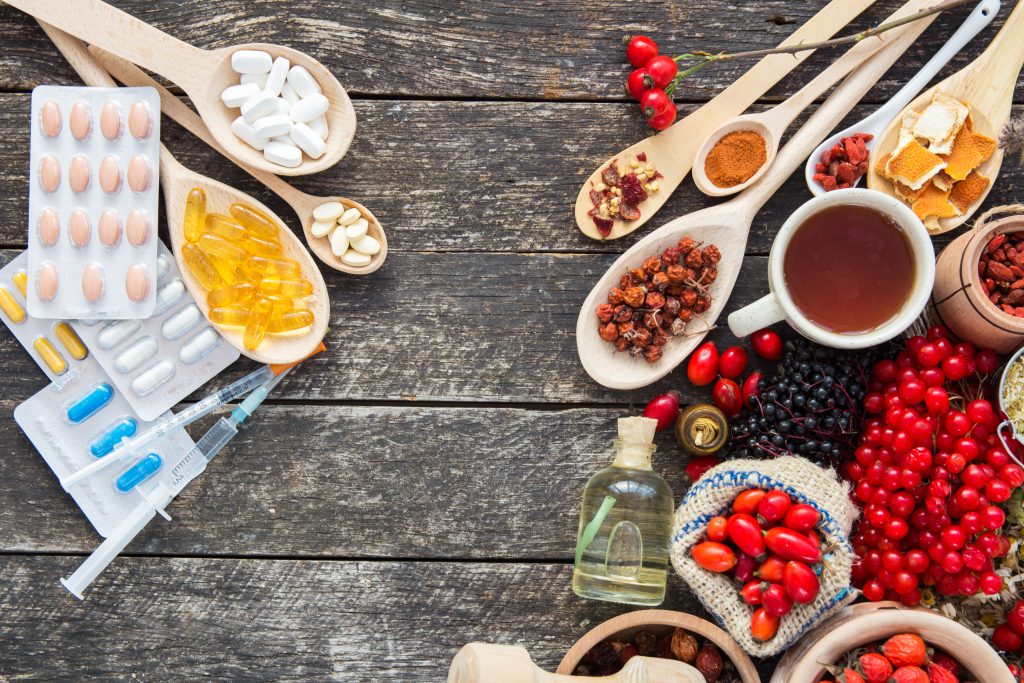 Schulmedizin in Form von Tabletten und Spritzen links, Naturmedizin in Form von Beeren, Gewürzen und Ölen rechts.