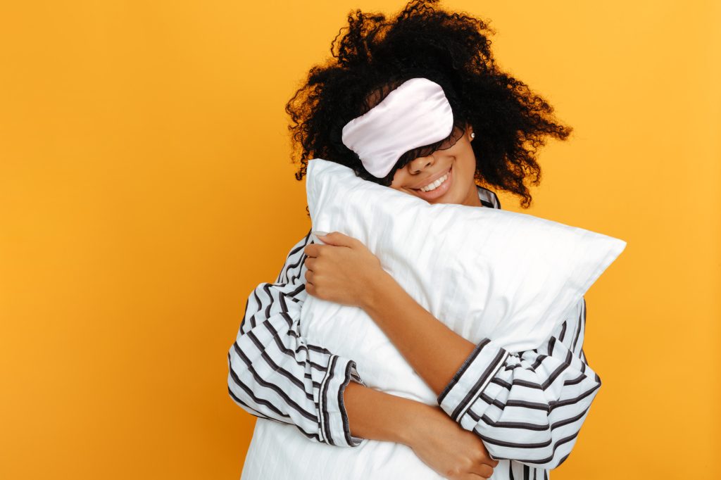 Junge Frau in Schlafanzug mit Schlafmaske und Kissen - Ayurveda gegen Stress