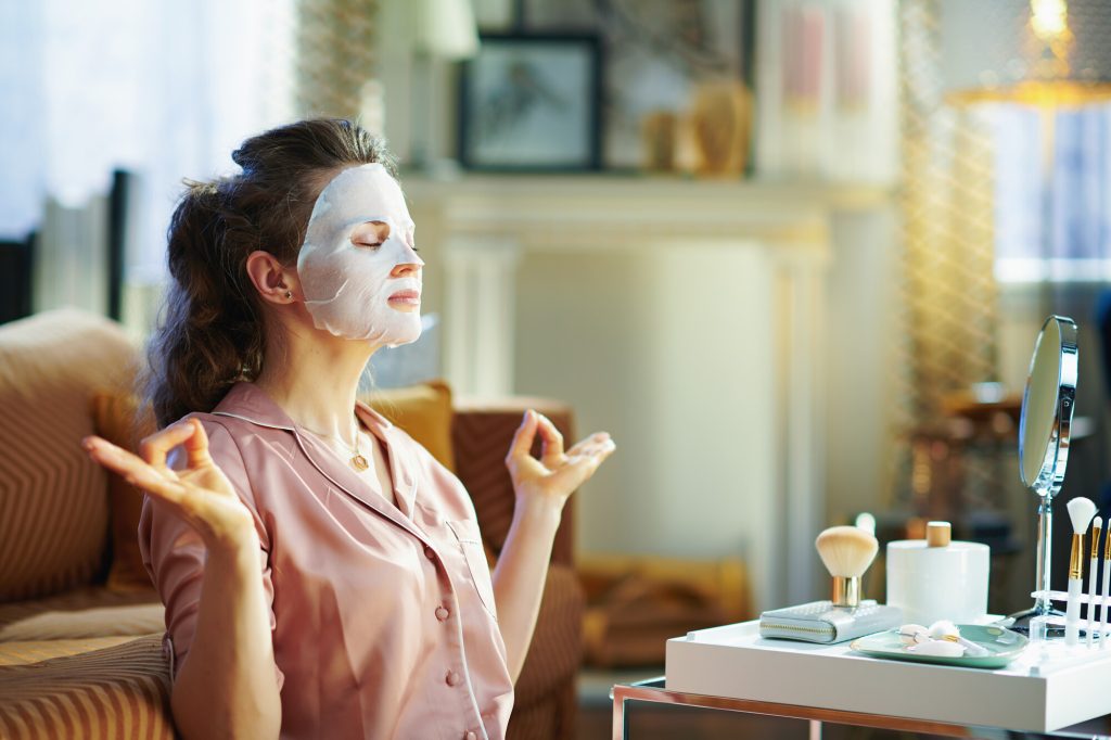 Junge Frau im Schlafanzug entspannt mit Gesichtsmaske - Ayurveda gegen Hautkrankheiten.