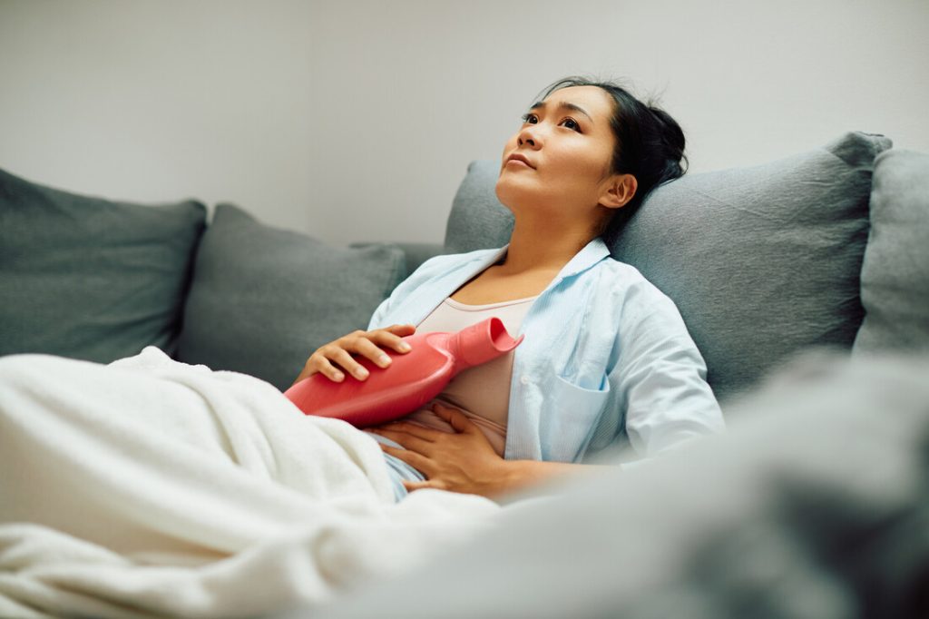 Frau mit Wärmflasche auf dem Sofa