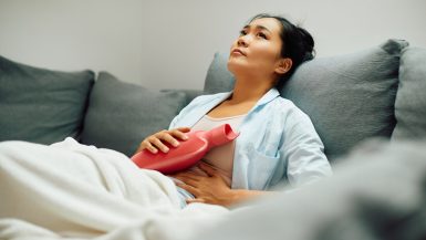 Frau mit Wärmflasche hat Bauchschmerzen