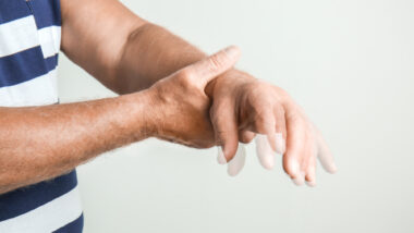 Alter Mann mit Parkinson hält sich die Hand