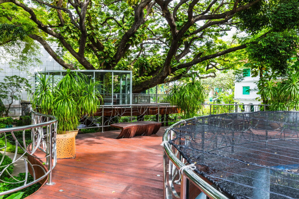 Holzweg in Sultan Park, mit Bänken und künstlerischen Verzierungen, im Hintergrund exotische Pflanzen und Bäume, die diesen Park zu einer der top 12 Sehenswürdikgeiten auf den Malediven machen.