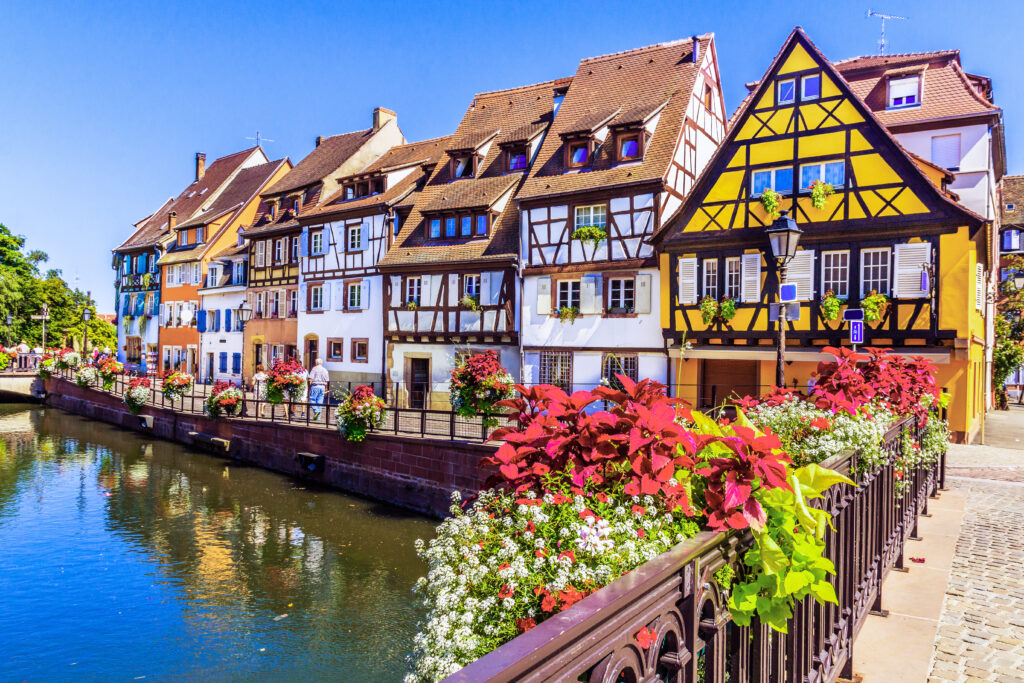 Bunte Fachwerkhäuser in Colmar, an einer Brücke über einen Kanal, Geländer sind mit Blumenkörben dekoriert