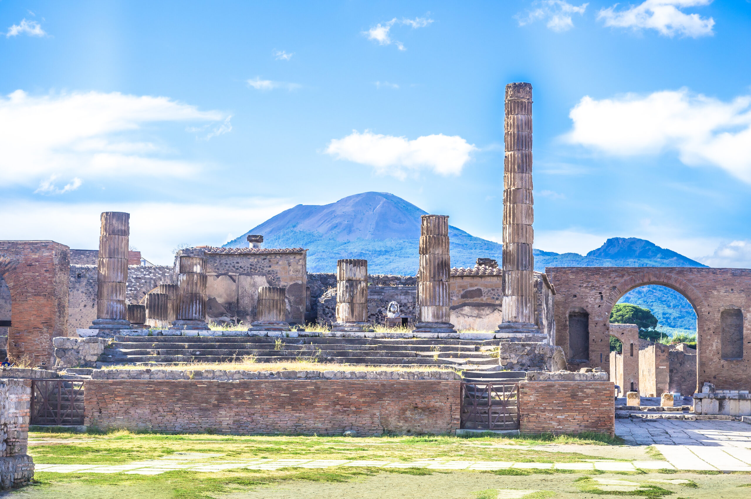 Ruinen der Sehenswürdigkeit Pompeji, abgebrochene Säulen ragen in die Höhe, im Hintergrund Berge und Hügel