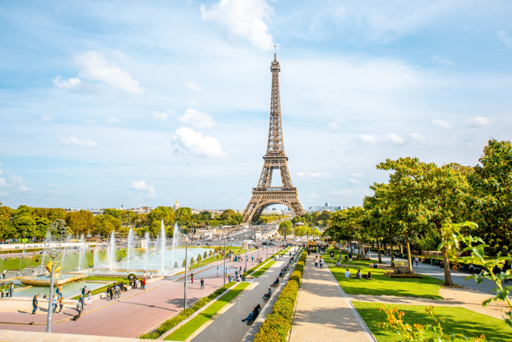 Der Eiffelturm in Paris zentral im Bild, davor befindet sich ein Park mit Springbrunnen