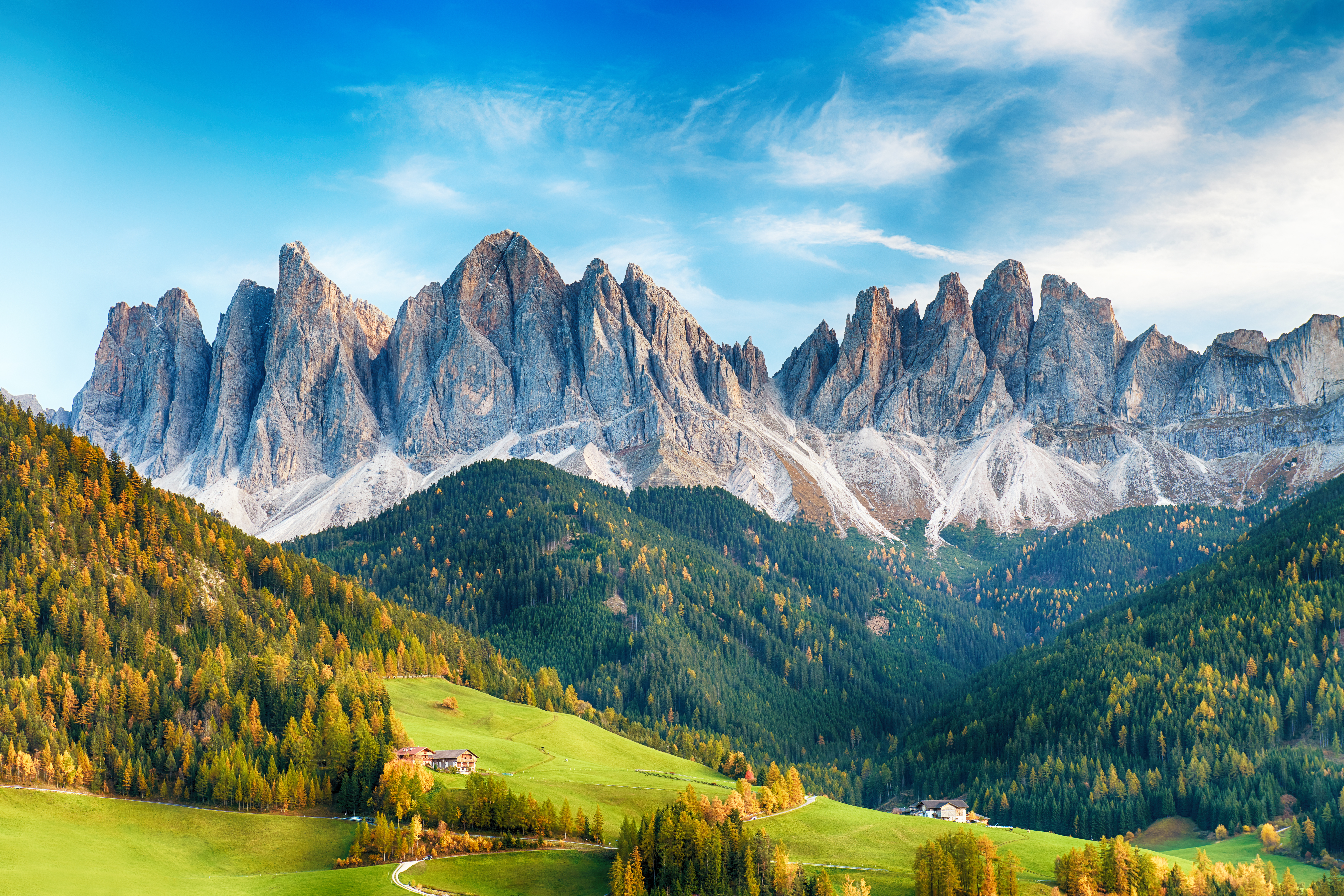 Zackige Felsformationen der Dolomiten ragen über grünen Hügeln mit Wäldern empor