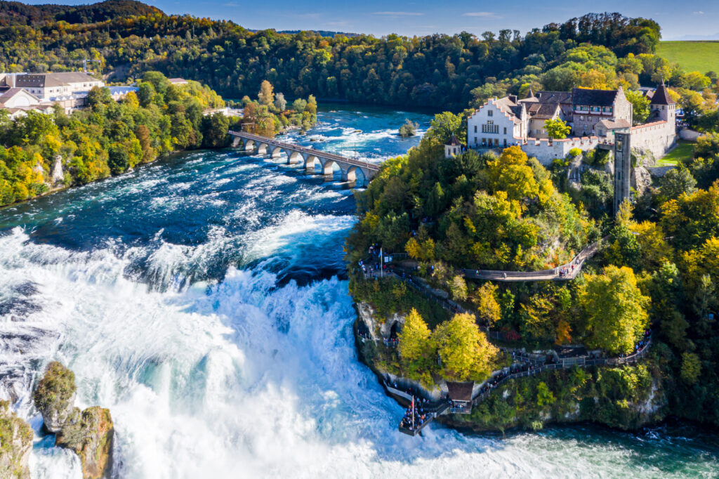 Der Rhein, der in den Rheinfall übergeht, brausende Wassermengen, rechts unten im Bild sieht man Menschen auf einer Aussichtsplattform, beliebte Sehenswürdigkeit in der Schweiz 