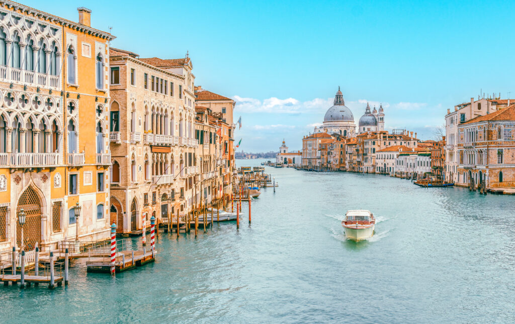 Der Canal Grande in Venedig, ein breiter Kanal mit einem Boot und orangen Häuserfassaden, mit Bootsanlegern am Ufer 
