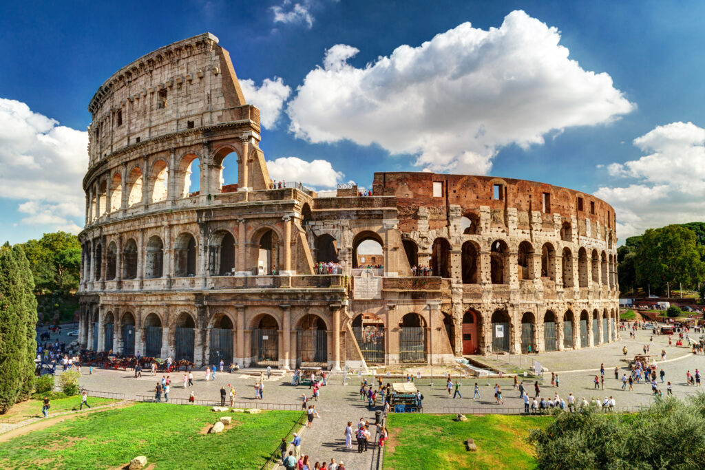 Bekannteste Sehenswürdigkeit in Italien, das Kolosseum in Rom, rundes Amphitheater mit einer Fassade aus mehreren Etagen aus Rundbögen, davor Touristen
