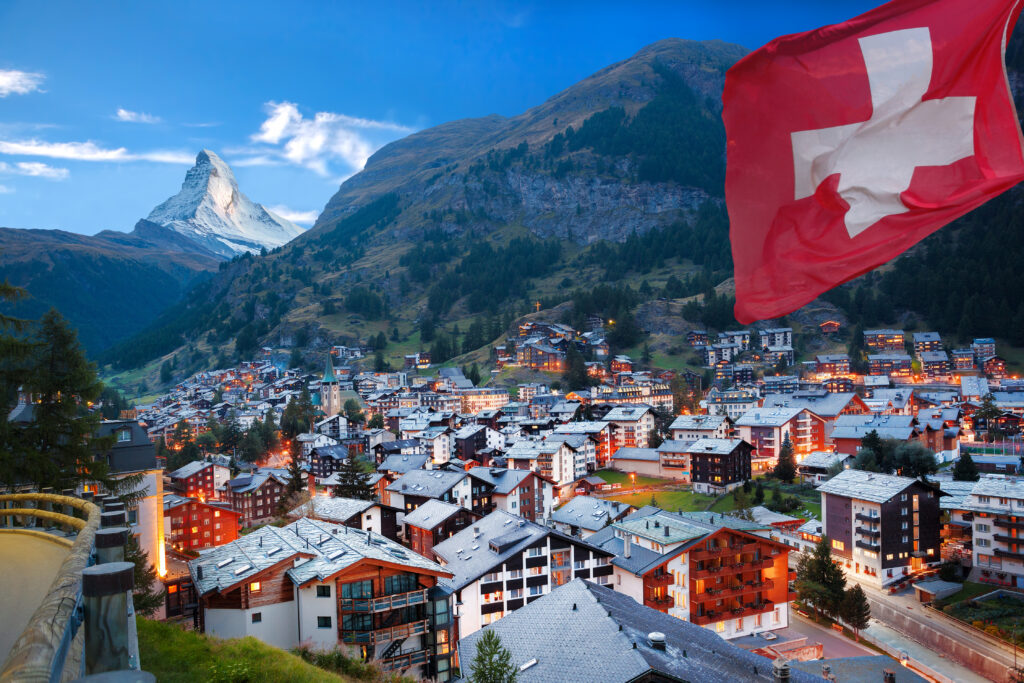 Das Dorf Zermatt mit Holzhäusern und dem Matterhorn im Hintergrund, rechts im Bild weht eine große Schweizer Flagge, beliebter Ferienort und Sehenswürdigkeit in der Schweiz