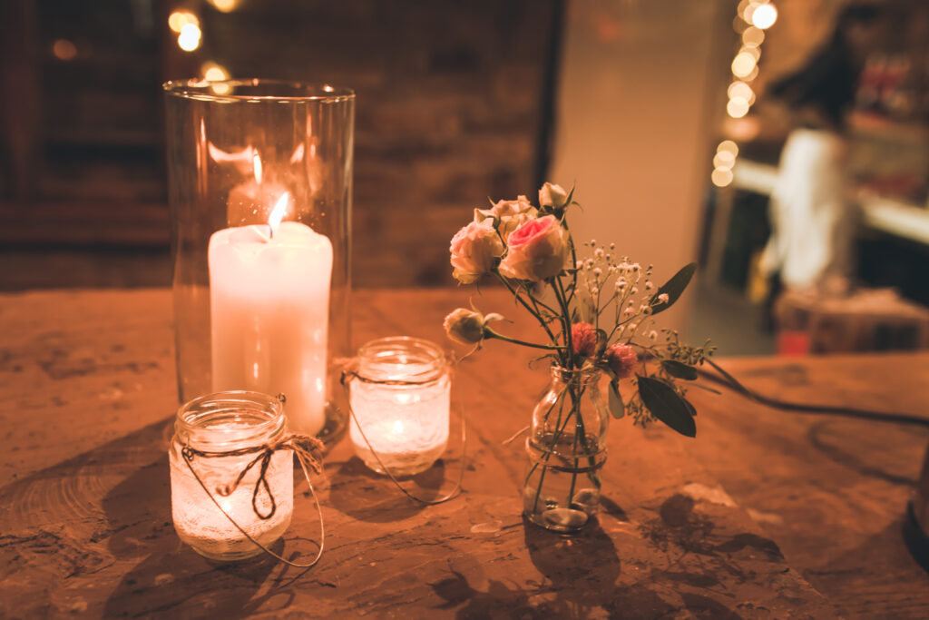 Kerzen und Blumendekoration, im Hintergrund sieht man Lichterketten in dem Raum