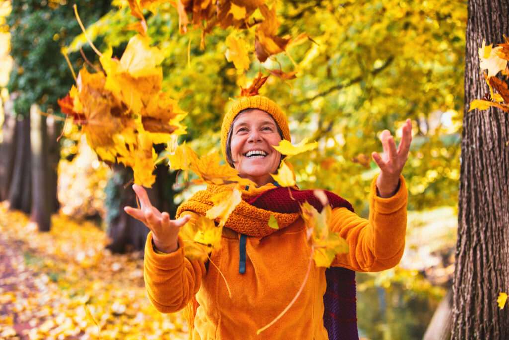 Eine Frau wirft glücklich Herbstlaub in die Luft