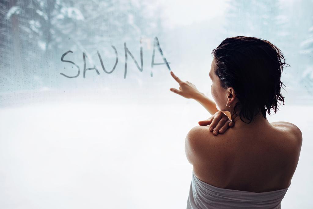 Eine Frau schreibt das Wort "SAUNA" an ein beschlagenes Fenster