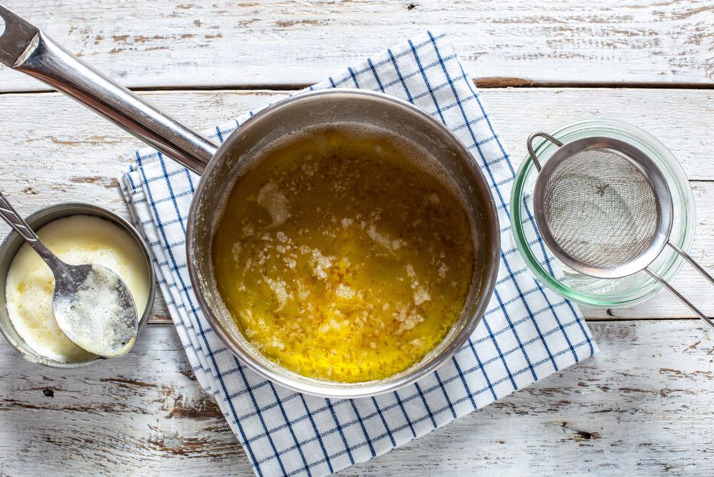 Topf mit Butter, Sieb und eine Schüssel mit abgeschöpftem Milcheiweiß