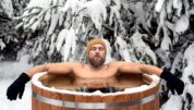 Ein Mann in einer Eistonne vor einer verschneiten Tanne.
