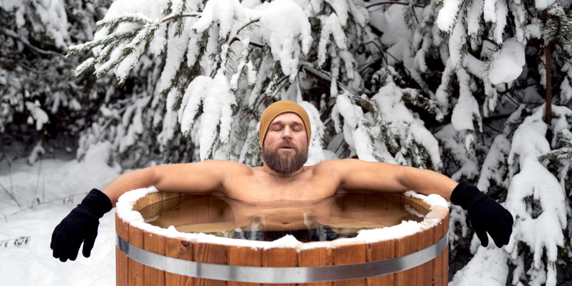 Ein Mann in einer Eistonne vor einer verschneiten Tanne.