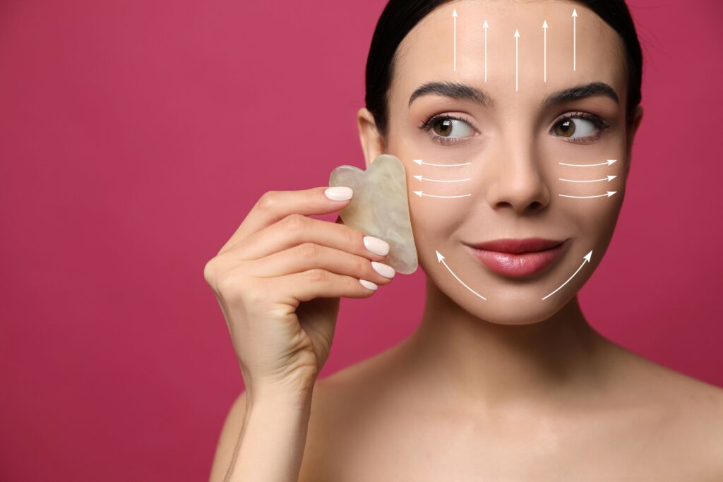 Eine Frau massiert ihr Gesicht mit einem Gua Sha Stein, entlang in weiß eingezeichneter Linien